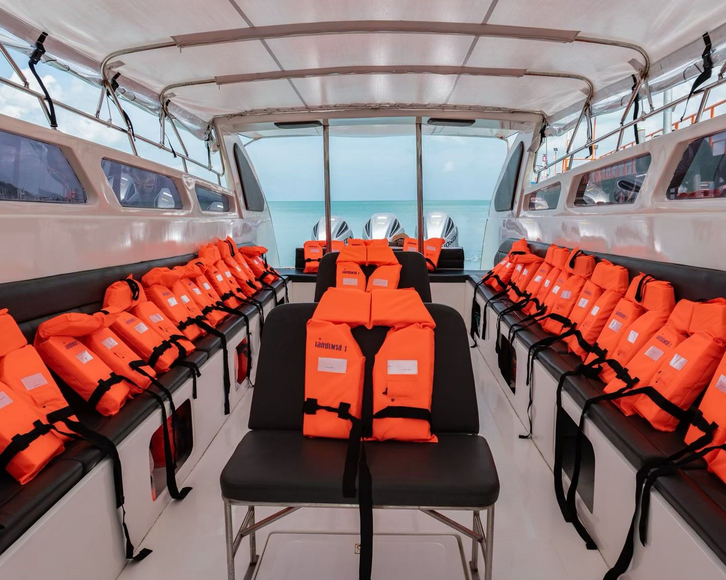 Leere Speedboot-Kabine mit orangen Rettungswesten auf schwarzen Sitzbänken, Meer und Außenborder achtern
