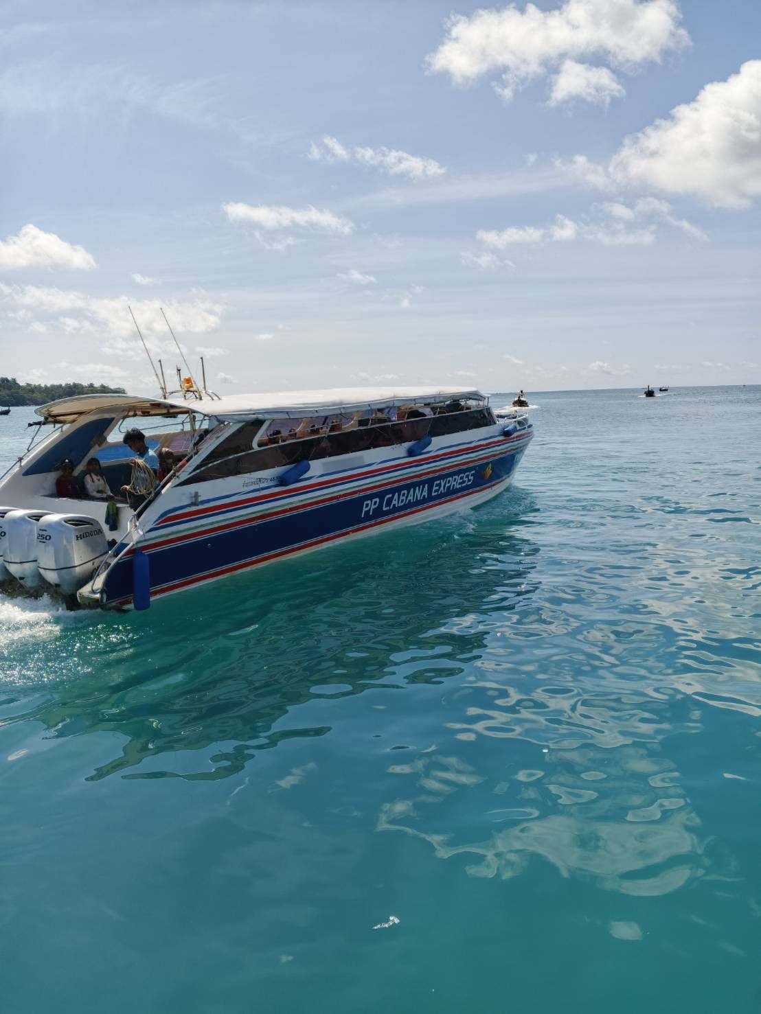 Blue and white "PP Cabana Express" speedboat carrying passengers across turquoise tropical water under a partly cloudy sky.