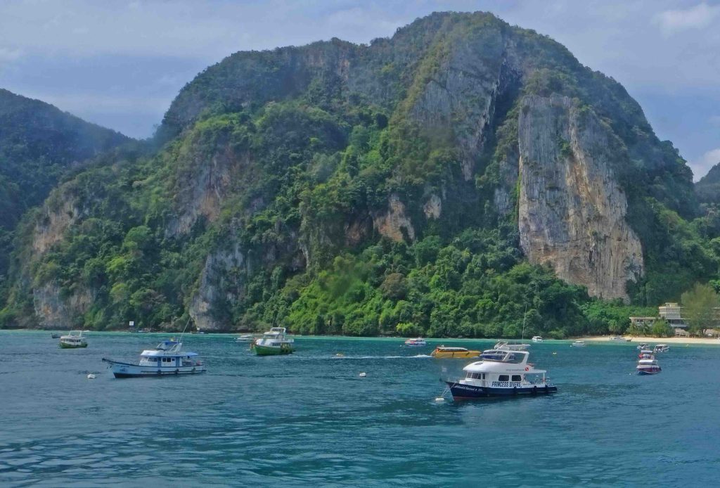 Turquoise bay with moored fishing boats and limestone cliffs covered in lush green vegetation