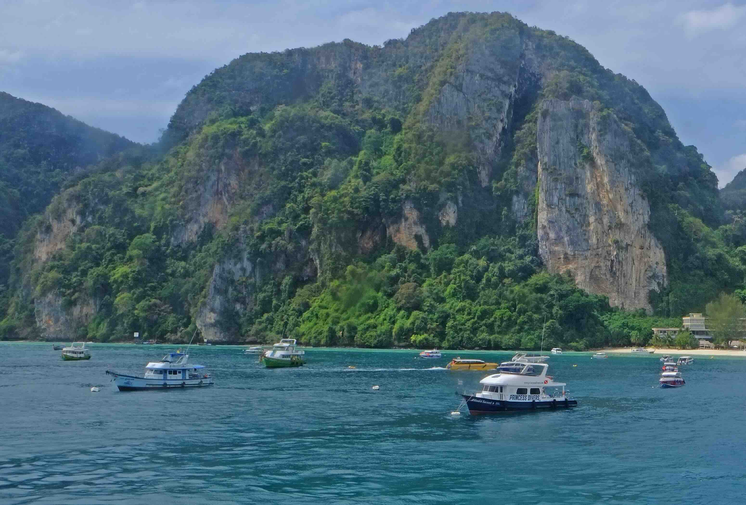 Turquoise bay with moored fishing boats and limestone cliffs covered in lush green vegetation