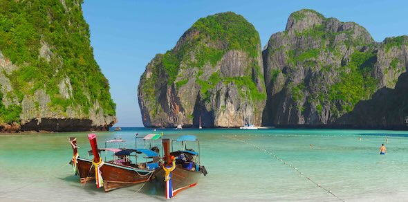 Traditional Thai longtail boats moored on white sand at Maya Bay, with turquoise water and limestone cliffs