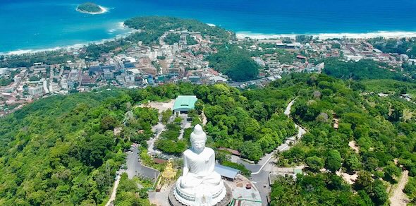 Aerial view of Phuket's white marble Big Buddha on a forested hilltop above town and turquoise coastline