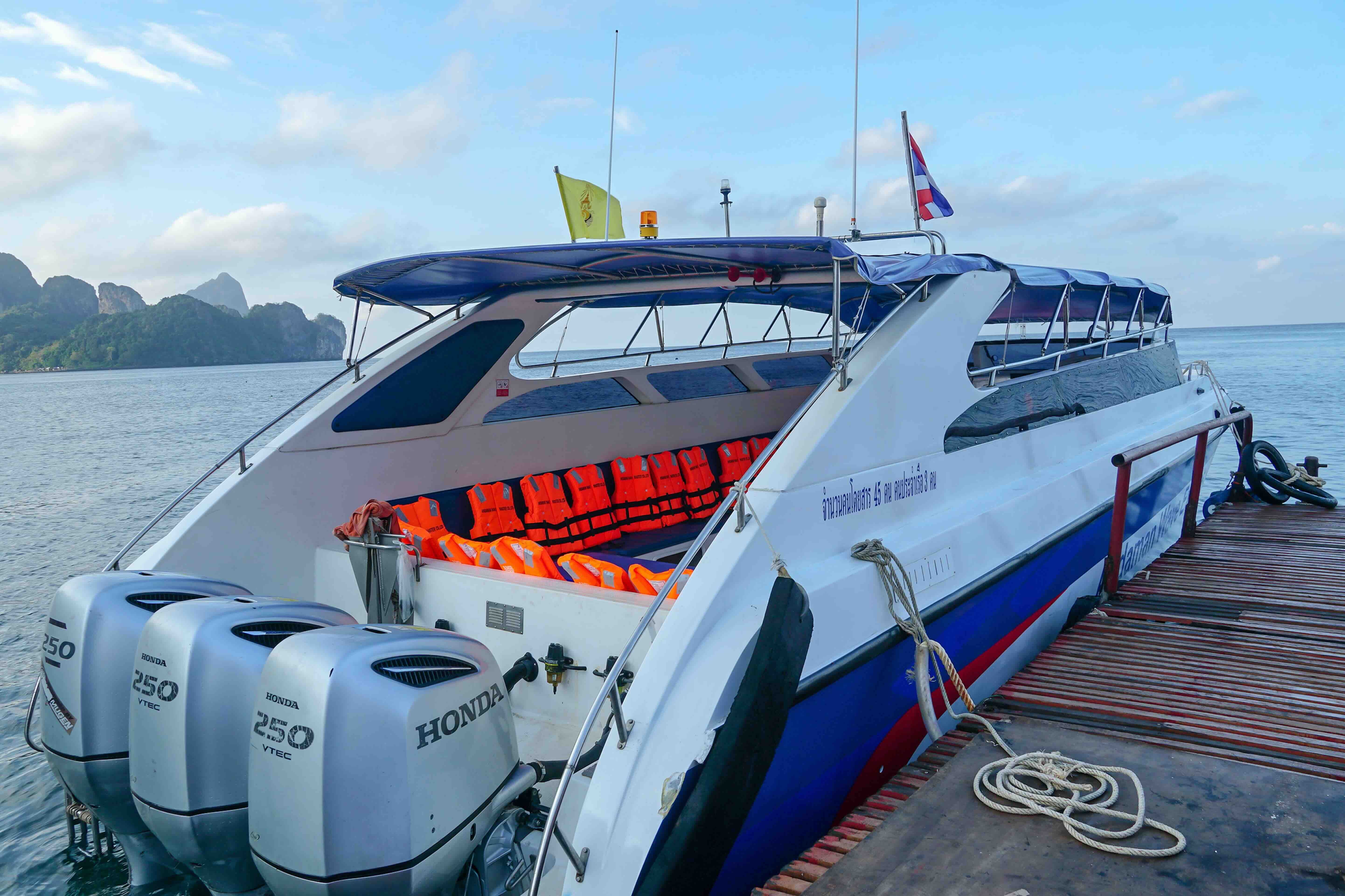 White and blue speedboat with three Honda 250 outboard motors moored at a wooden pier, orange life jackets on board