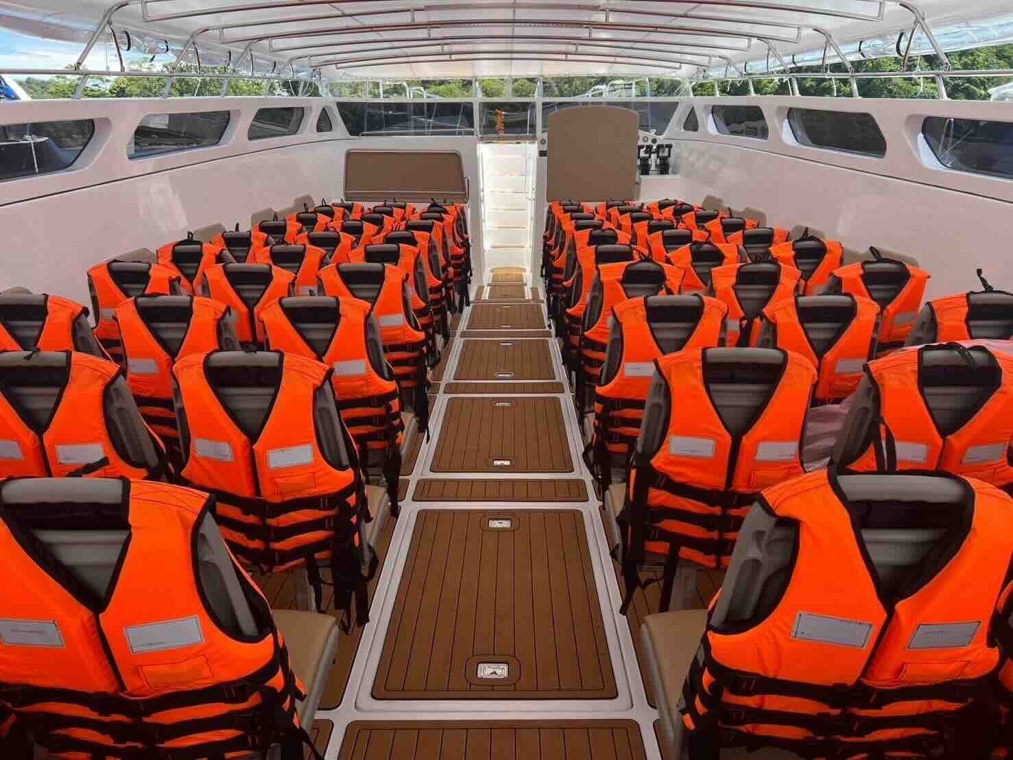 Leere Passagierkabine eines Speedboots mit Sitzreihen voller orangefarbener Rettungswesten und Gang in Teakoptik