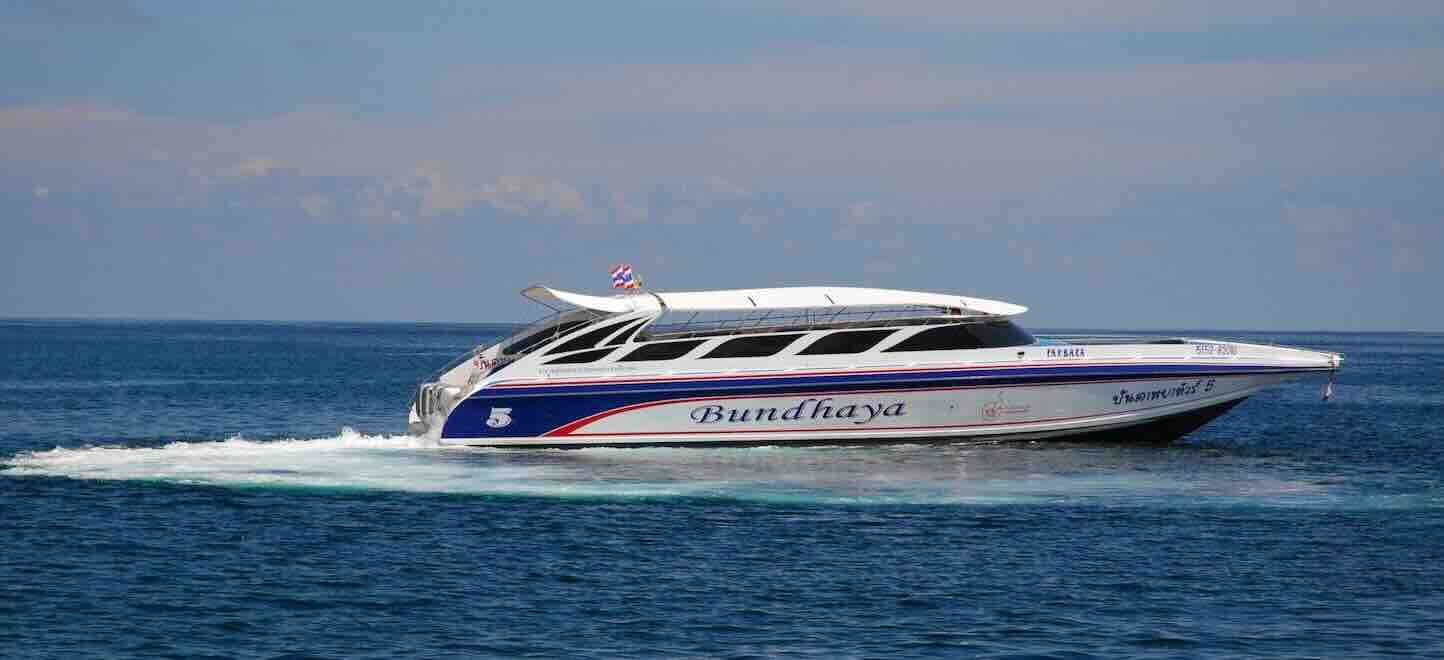 Weißes Bundhaya-Speedboot mit blauen und roten Streifen fährt über offene blaue See unter diesigem Himmel