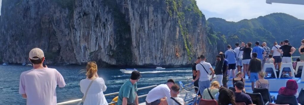 Tourists on a ferry boat viewing dramatic limestone cliffs rising from turquoise water