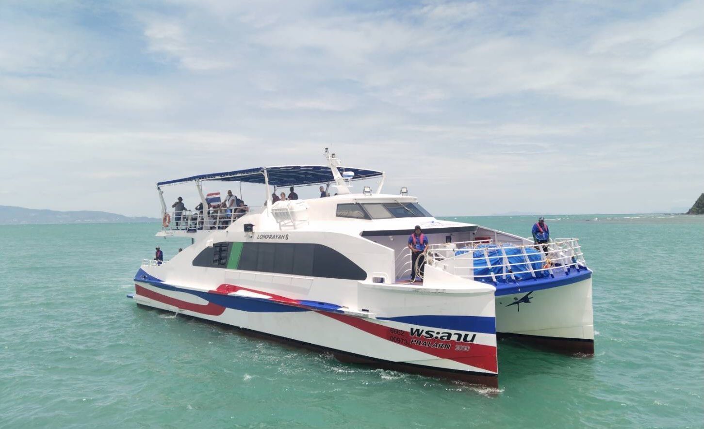 White high-speed catamaran ferry "Lomprayah 8" with red and blue hull stripes on calm turquoise sea, passengers on upper deck