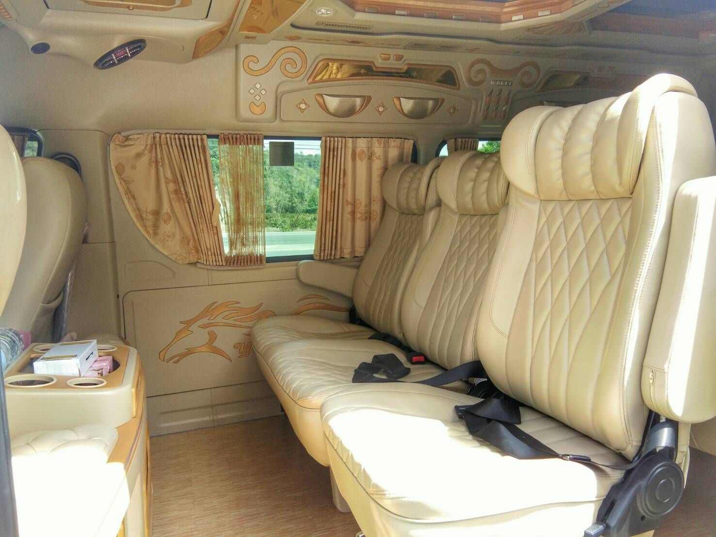 Interior of a VIP minivan with cream leather reclining seats, gold trim, curtained windows and cup holders