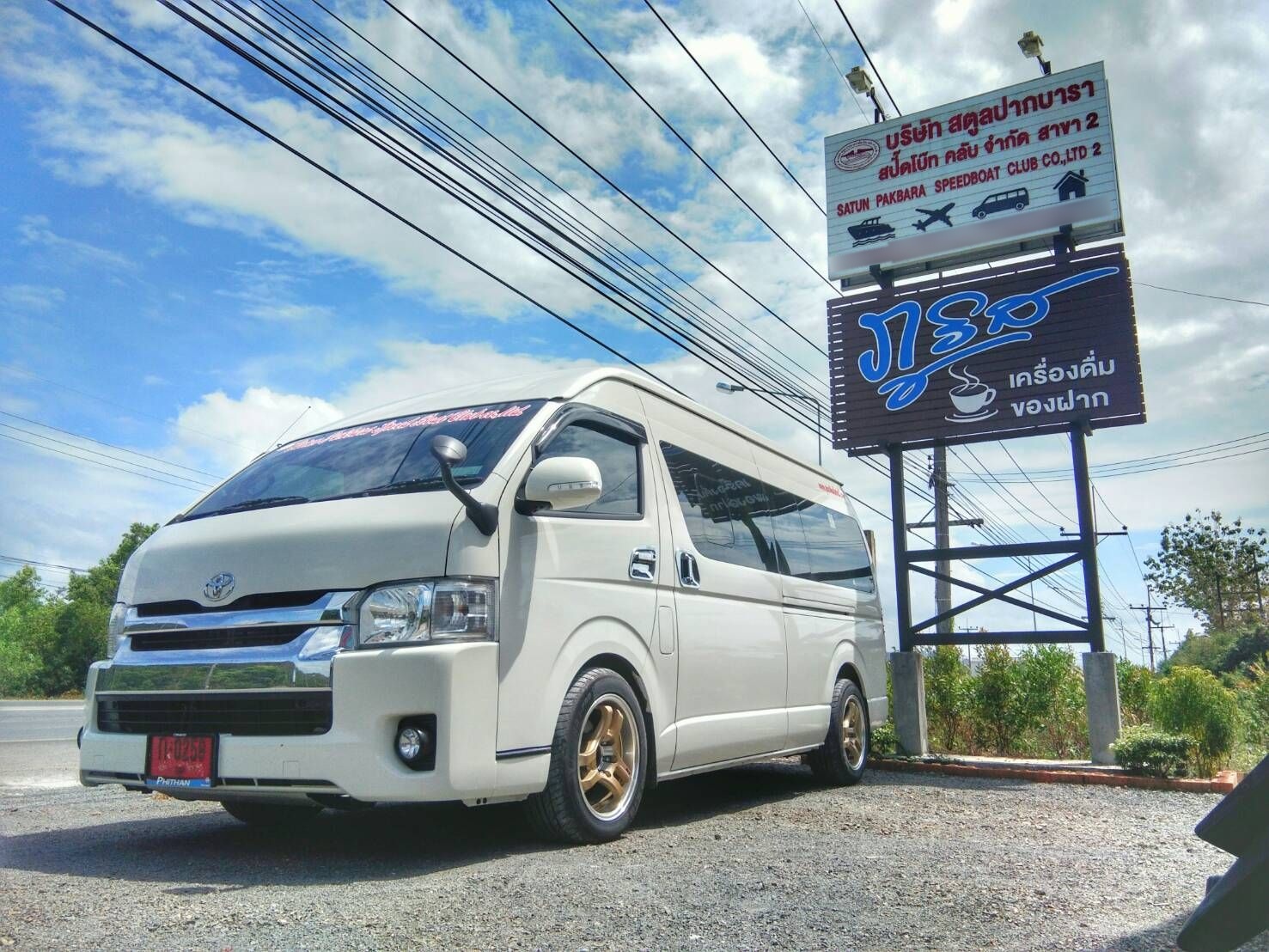 White Toyota Hiace minivan parked on gravel beside a Satun Pakbara Speedboat Club roadside sign in Thailand