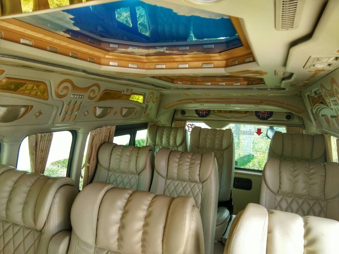 Interior of a minivan with quilted beige leather seats, decorative ceiling panels and blue-tinted skylight