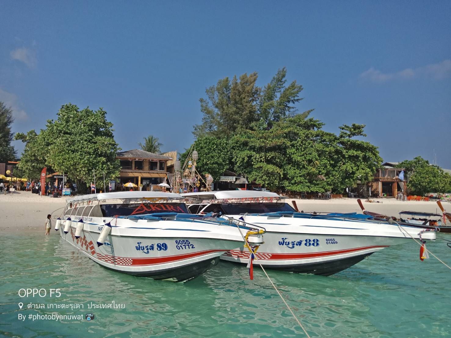 Zwei weiße Speedboote im türkisen Flachwasser vor einem thailändischen Inselstrand mit Bäumen und Strandbars