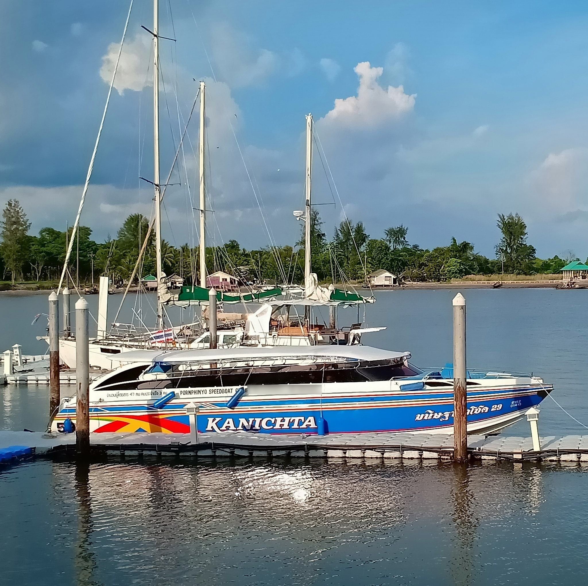 Blau-weiße Schnellbootfähre „Kanichta“ an schwimmendem Pontonsteg neben Segelbooten in Thailand