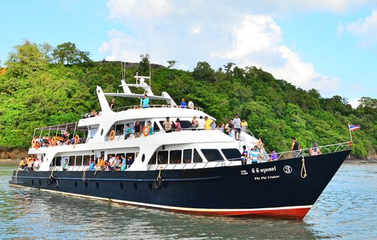 Passagierboot Phi Phi Cruiser mit Touristen an Deck fährt unter blauem Himmel an bewaldeter Insel vorbei