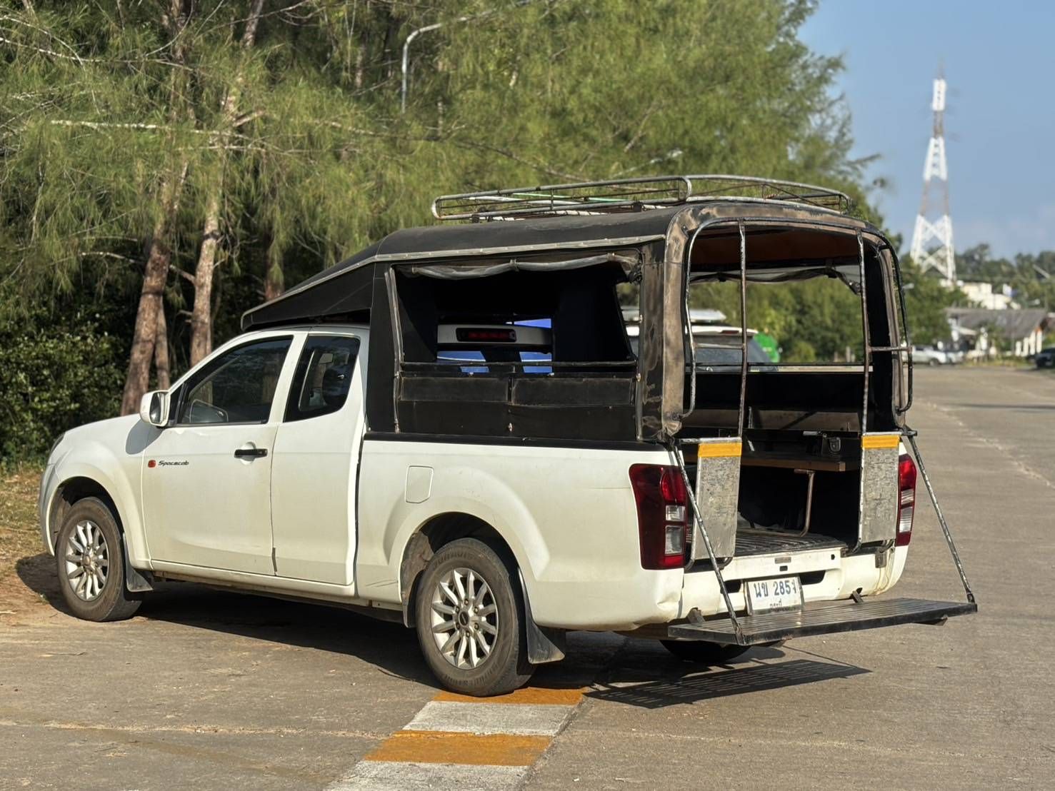 Weißer Pickup, umgebaut zum Songthaew-Sammeltaxi mit Sitzbänken und Dachträger, am Straßenrand geparkt