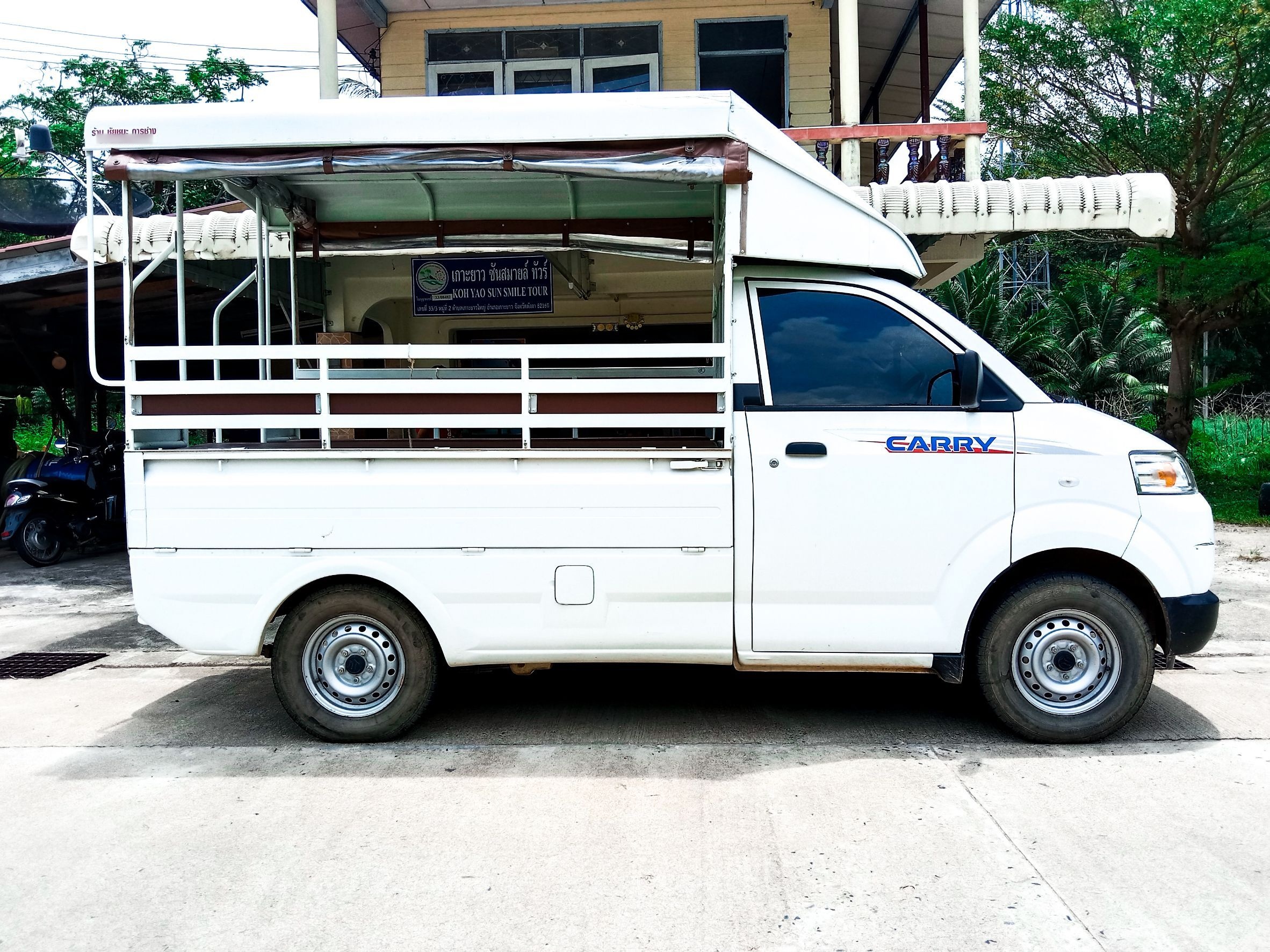 Weißer Suzuki Carry Songthaew mit Sitzbänken und Verdeck vor einem Tourbüro auf Koh Yao