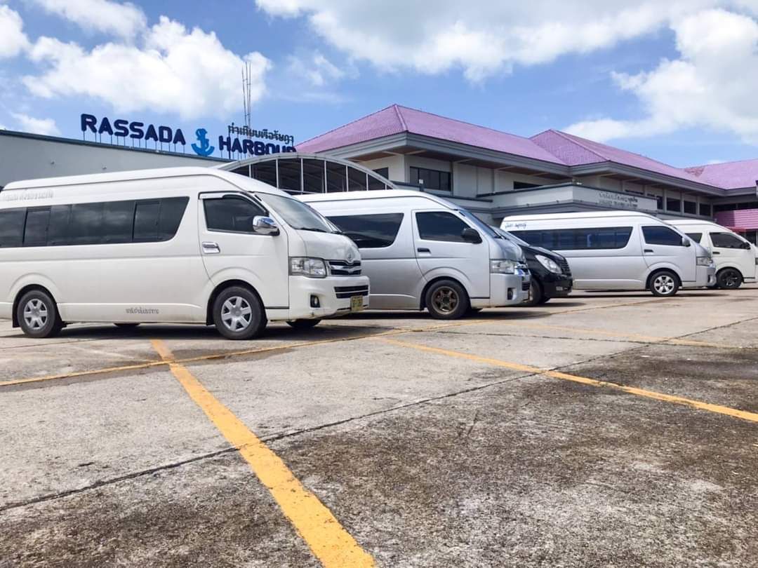 Reihe weißer Minivans auf Betonplatz vor dem Fährterminal Rassada Harbour in Phuket unter blauem Himmel