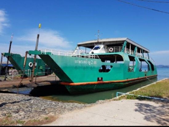 Grüne thailändische Autofähre mit heruntergelassener Bugrampe an einer Betonslipanlage unter blauem Himmel