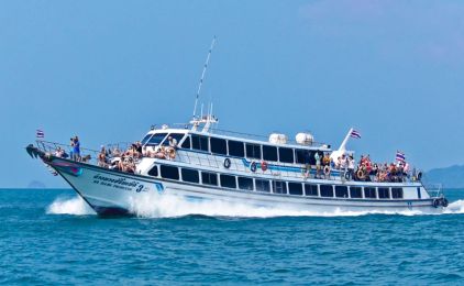 Crowded white passenger ferry with Thai flags cruising across turquoise sea near a forested island