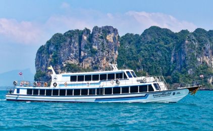 White double-deck passenger ferry anchored on turquoise water below limestone karst cliffs in southern Thailand