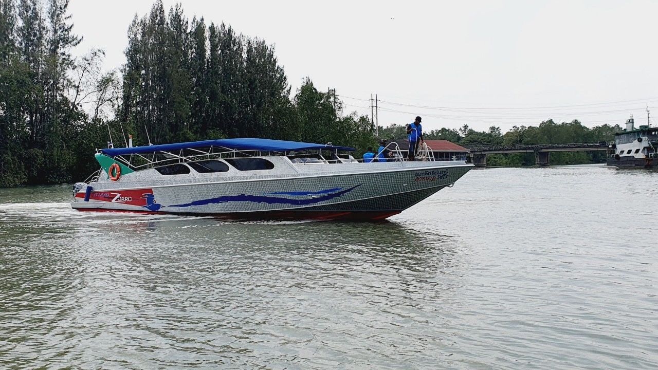 Aluminium speedboat with blue canopy cruising a calm river past mangroves, crew standing on deck