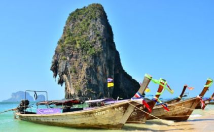 Traditionelle thailändische Longtailboote mit bunten Bändern am Strand vor einem hohen Kalksteinfelsen