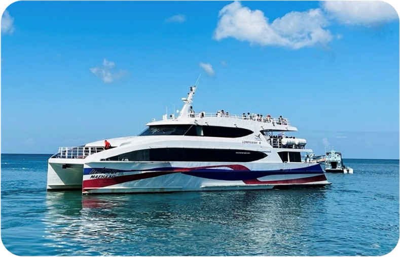 White high-speed catamaran ferry with red and blue hull stripes anchored on calm turquoise sea under blue sky