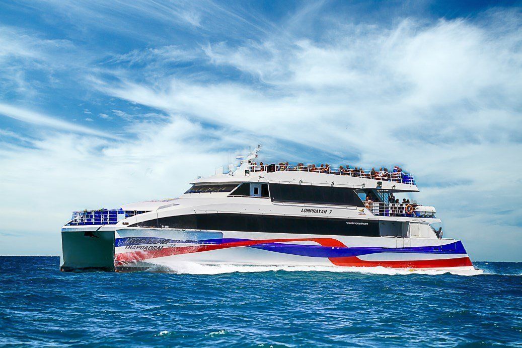 Lomprayah high-speed catamaran ferry with red, white and blue hull cruising on open blue sea under cirrus clouds