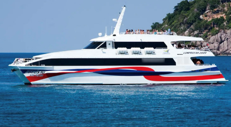 White high-speed catamaran ferry with red and blue hull stripes cruising past a rocky green island in blue sea