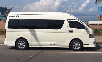 White minivan with Thai lettering parked on a roadside beside a beach and sea in Thailand