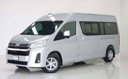 Silver Toyota Hiace passenger van parked in a bright indoor showroom, front three-quarter view