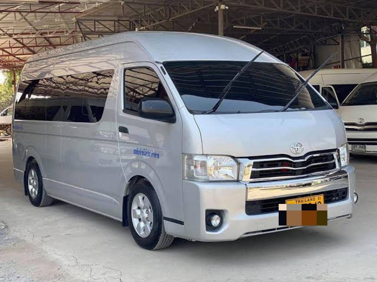 Silberner Toyota Hiace Hochdach-Kleinbus mit Thai-Kennzeichen in offenem Depot neben anderen Vans