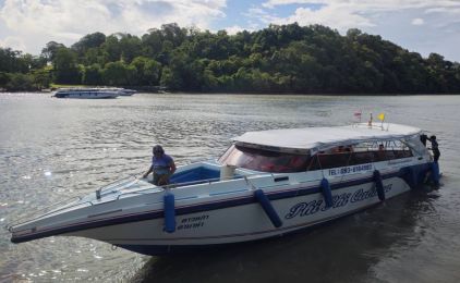 White and blue speedboat moored in calm water beside a forested headland, with a second speedboat offshore