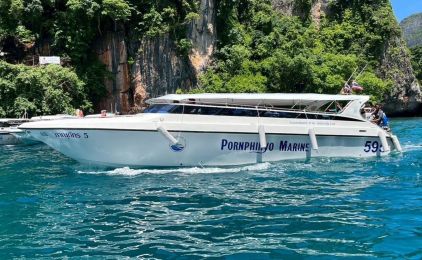 White speedboat marked "Pornphinyo Marine 599" moored on turquoise water below limestone cliffs in Thailand