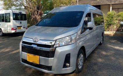 Silver Toyota Hiace passenger van with yellow commercial plate parked beside a white minibus