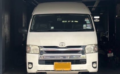 White Toyota Hiace minibus van parked front-on inside a dim garage with a yellow Thai licence plate