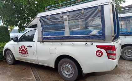 White pickup truck with covered passenger canopy and red number 6 decal parked on a paved lot beside greenery