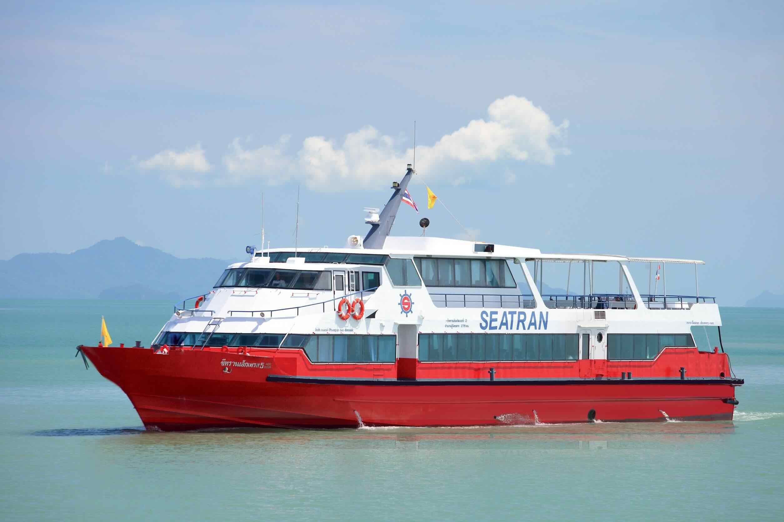 Красно-белый пассажирский паром Seatran идёт по спокойному зелёному морю, позади холмы острова в дымке