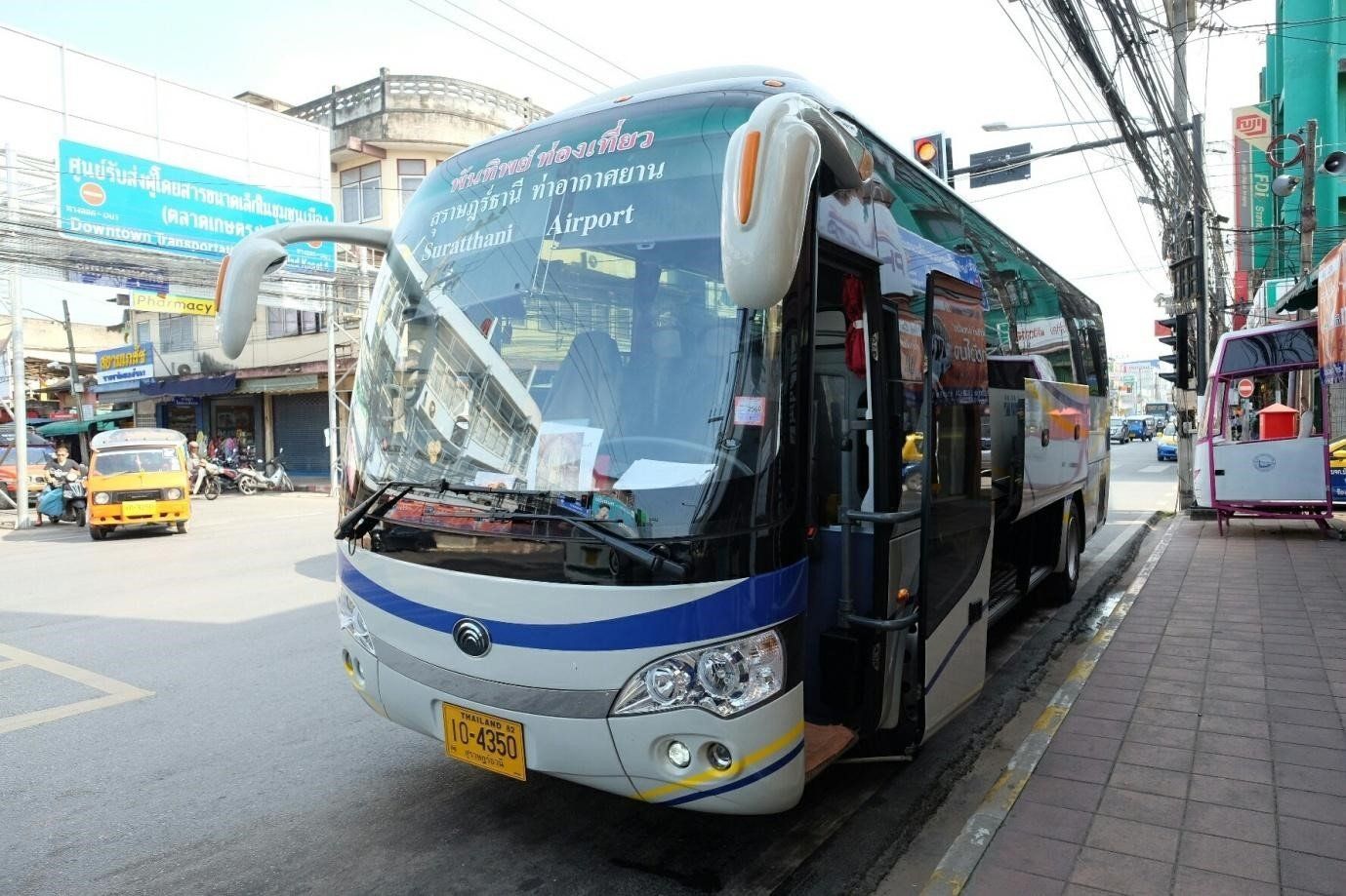 素叻他尼机场接驳巴士停在泰国街道上，身后可见嘟嘟车和店铺招牌