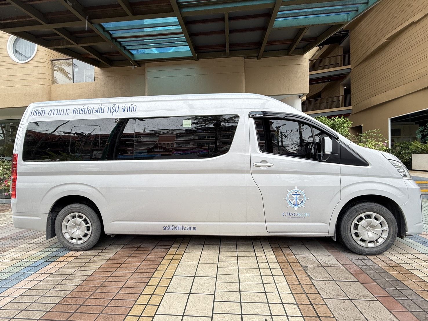 Weißer Toyota Hiace Minivan mit thailändischer Schrift und Anker-Logo der Chao Koh Corporation Group unter Hoteldach