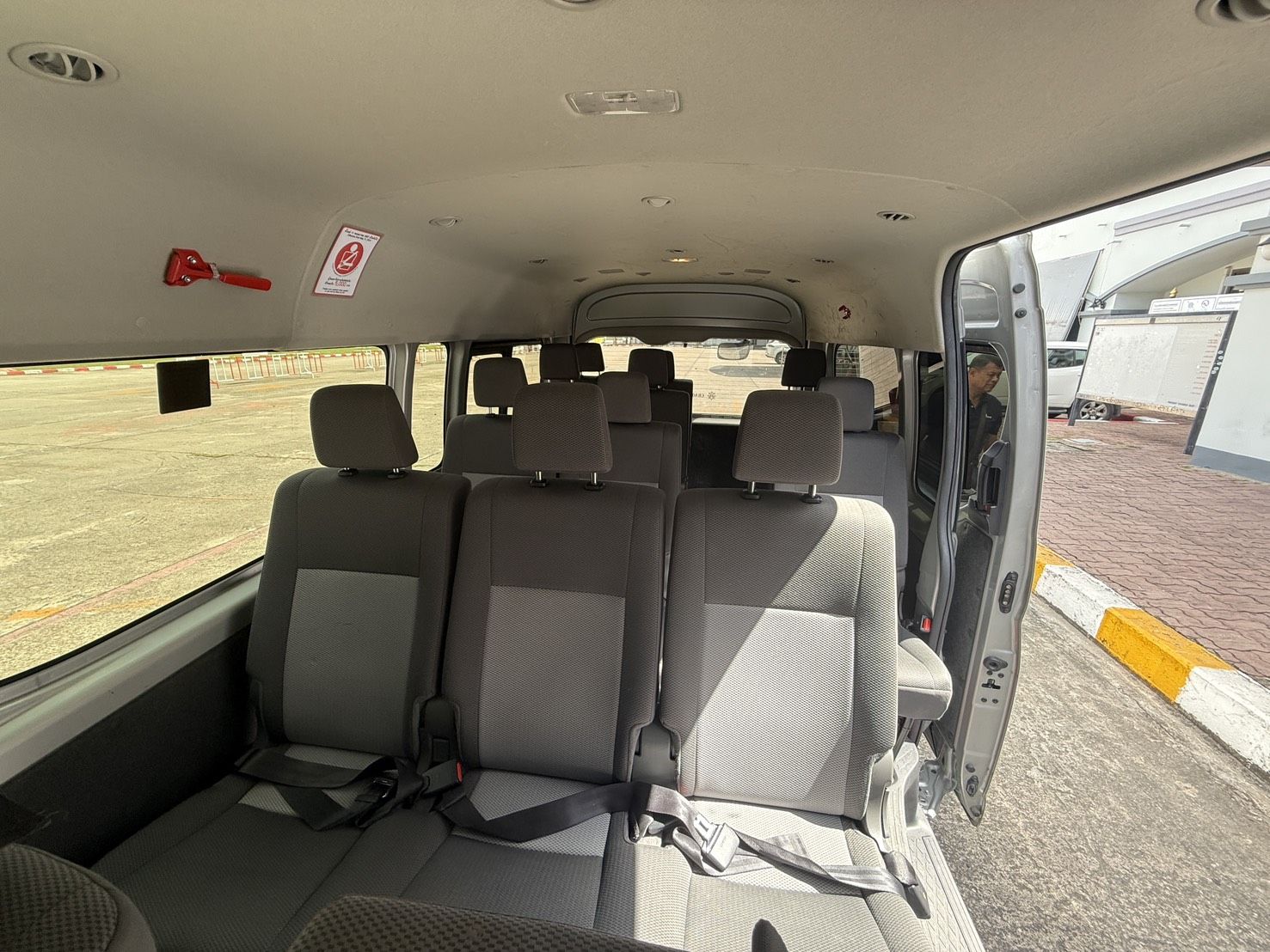 Leere graue Stoffsitze in einem Minivan, seitliche Schiebetür offen zum Parkplatz