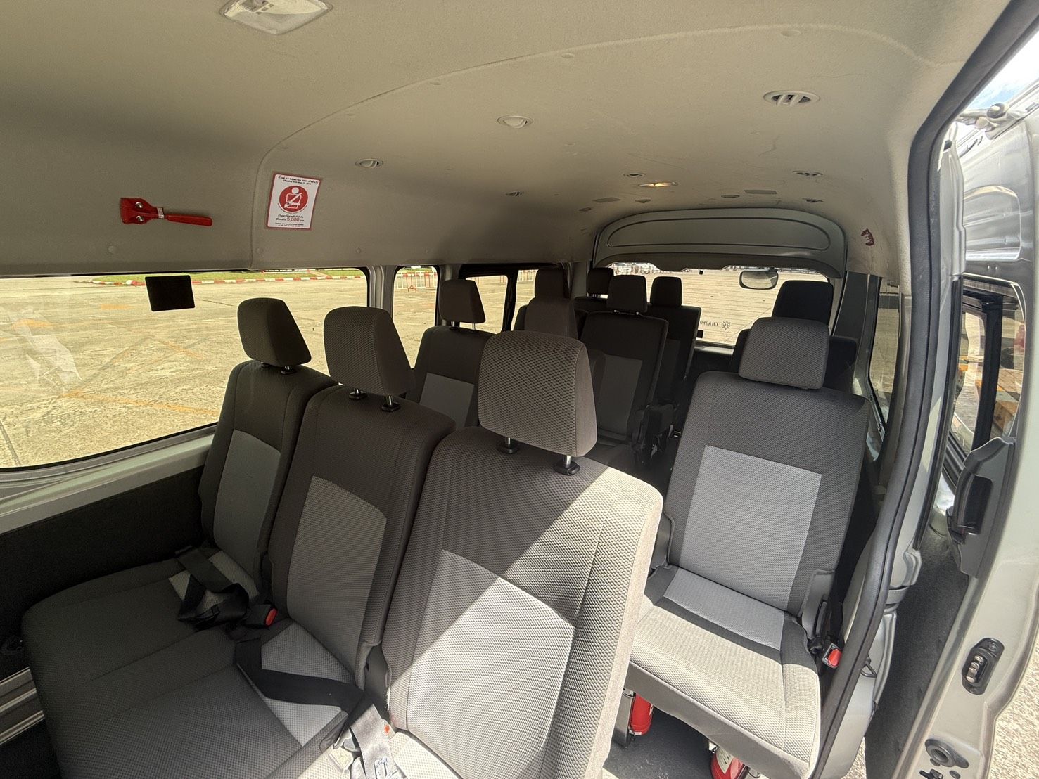 Innenraum eines leeren Minivans mit grauen Stoffsitzen und Gurten, Seitentür offen zum gepflasterten Platz