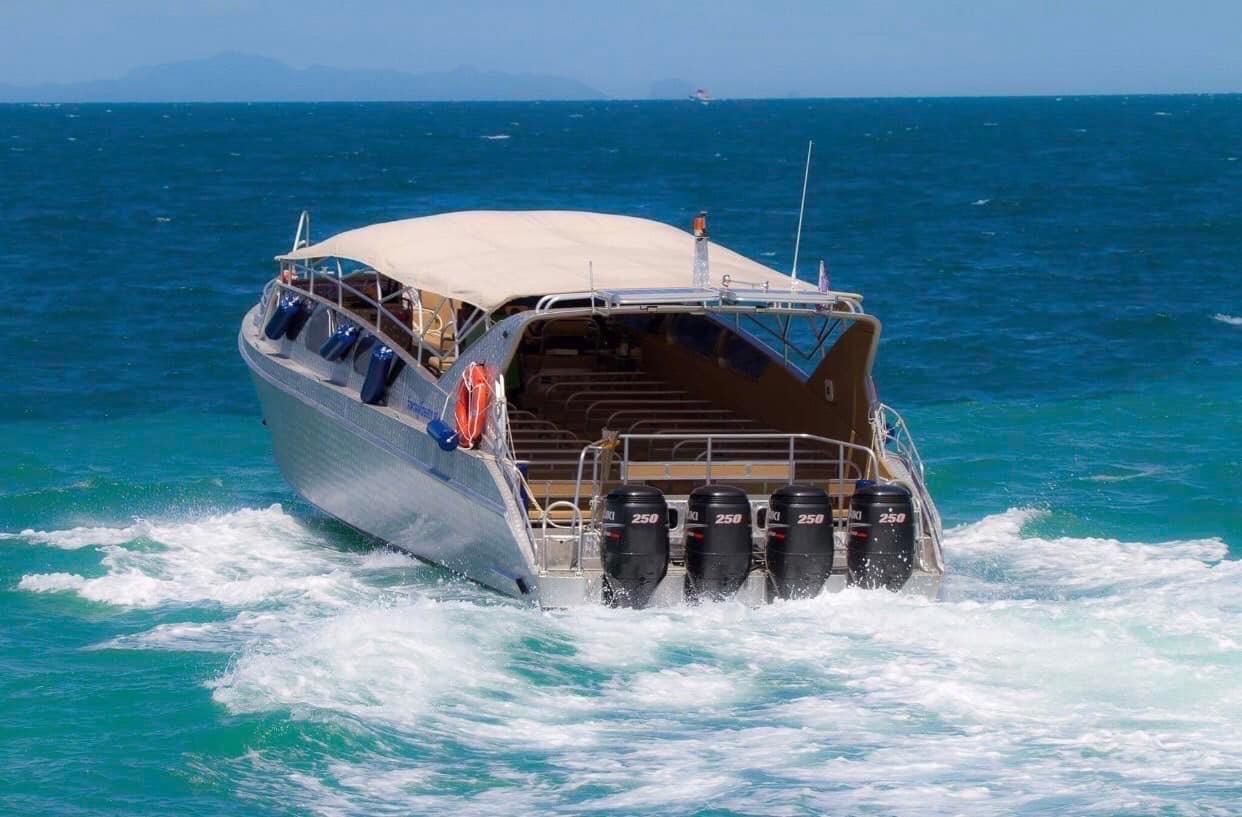 Speedboot mit beigem Verdeck und vier 250-PS-Außenbordern auf türkisem Meer, Inseln am Horizont
