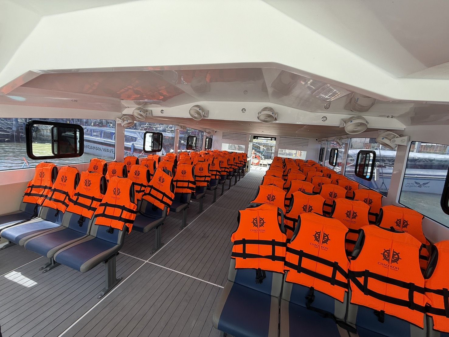 Leere klimatisierte Fährkabine mit Reihen blauer Sitze, über die orange Rettungswesten gelegt sind, und großen Fenstern