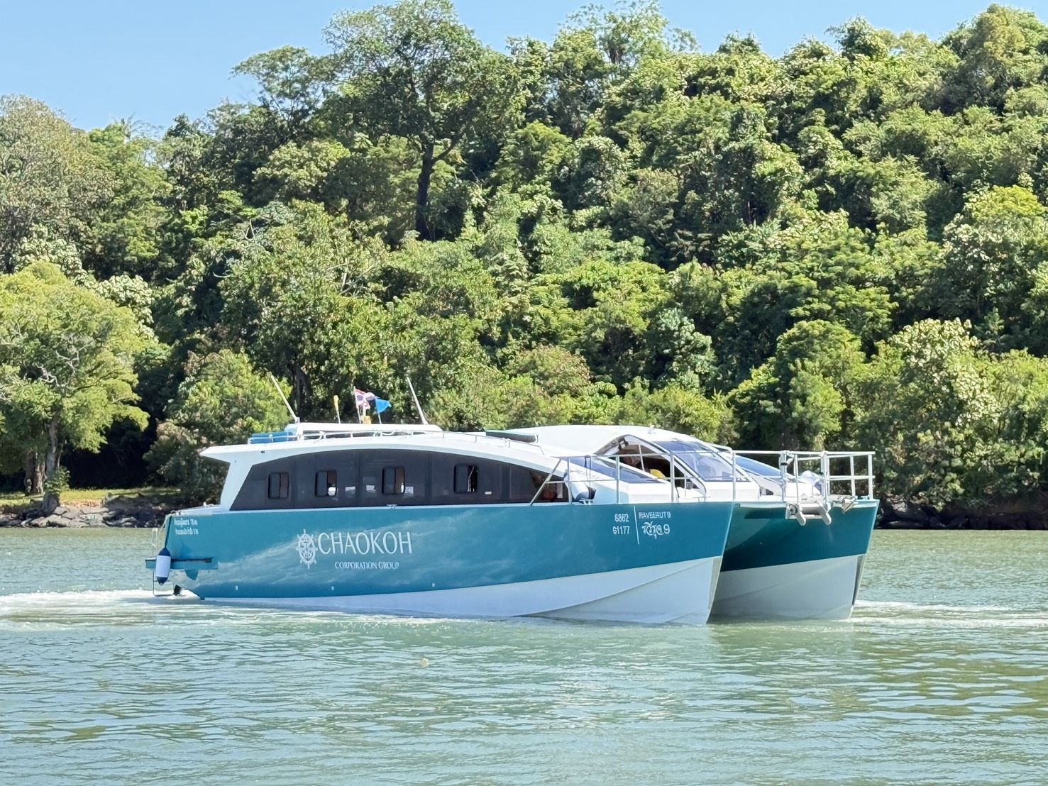 Türkis-weißes Chaokoh-Katamaran-Speedboot auf ruhigem grünem Wasser vor bewaldeter Inselküste