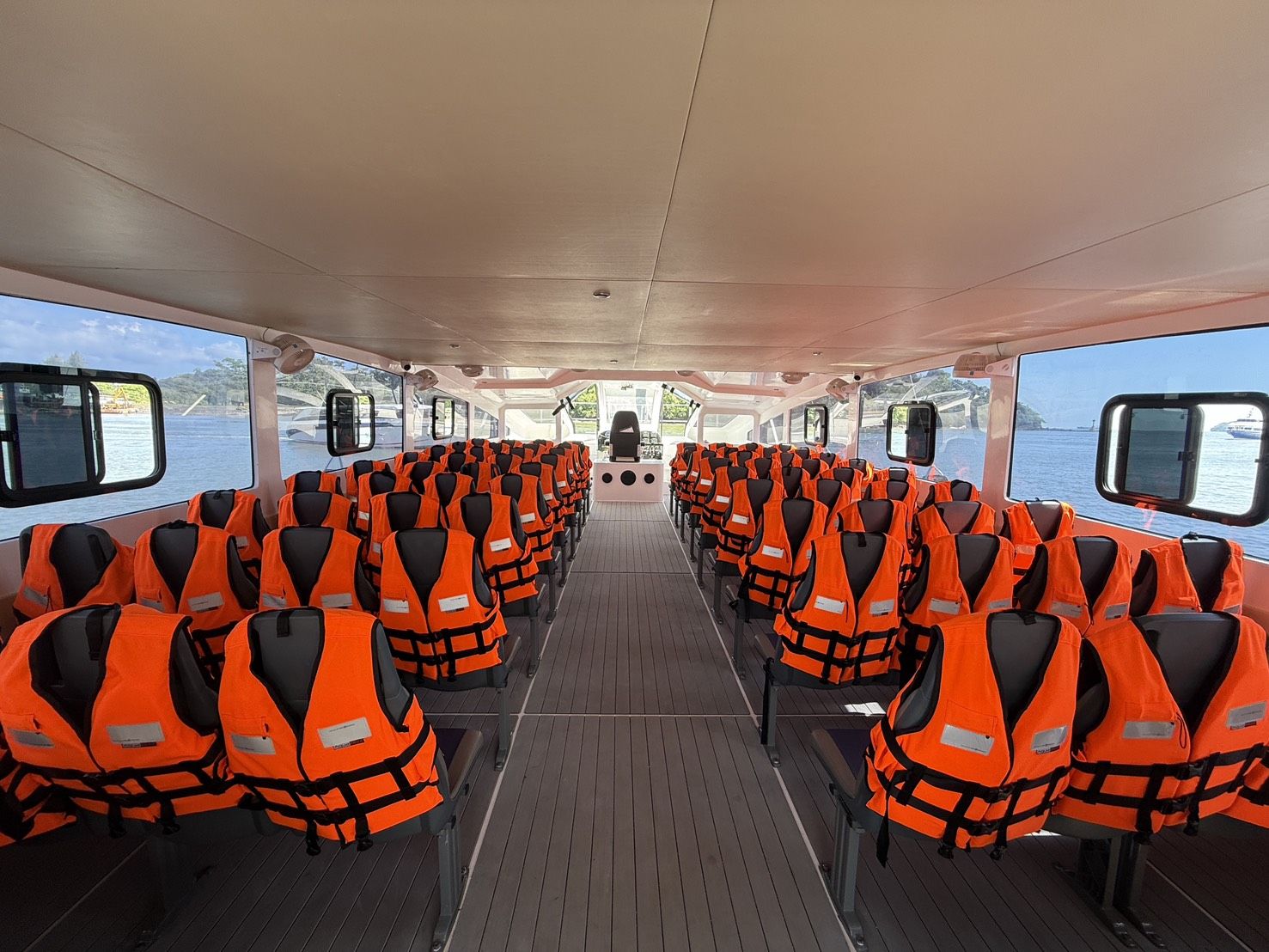 Leere Passagierkabine eines Speedboot-Fähre mit Sitzreihen voller orangefarbener Rettungswesten und Meerblick