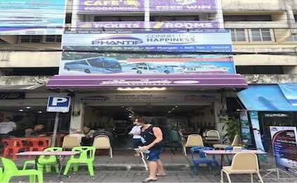 Colorful storefront with blue and purple signage, plastic chairs, and pedestrians on a Southeast Asian street