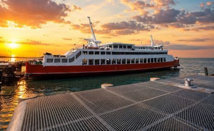 सूर्यास्त में धातु घाट रैंप पर लगी लाल-सफेद यात्री फेरी, शांत समुद्र पर नारंगी बादल