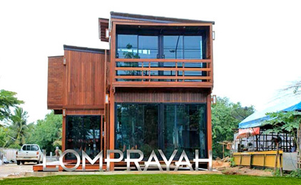 Modern stacked shipping container building with large windows and KOMPRAYAL signage on grass field