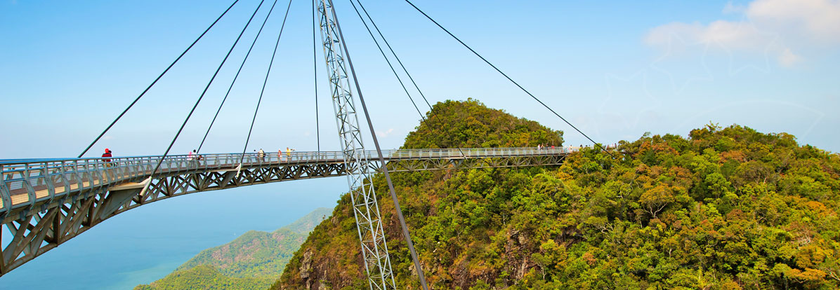 Curved pedestrian sky bridge on steel cable pylon spanning jungle-covered hills above a blue tropical sea