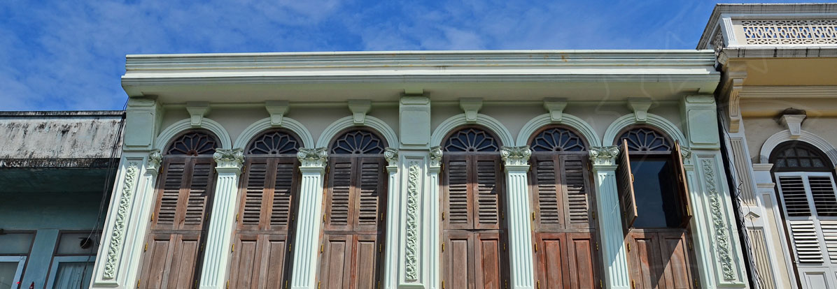Mint-green Sino-Portuguese shophouse upper facade with arched windows and wooden louvred shutters under blue sky